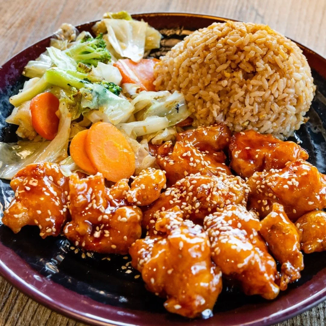 A plate of fried rice, vegetable stir-fry with carrots and cabbage, and orange chicken garnished with sesame seeds.