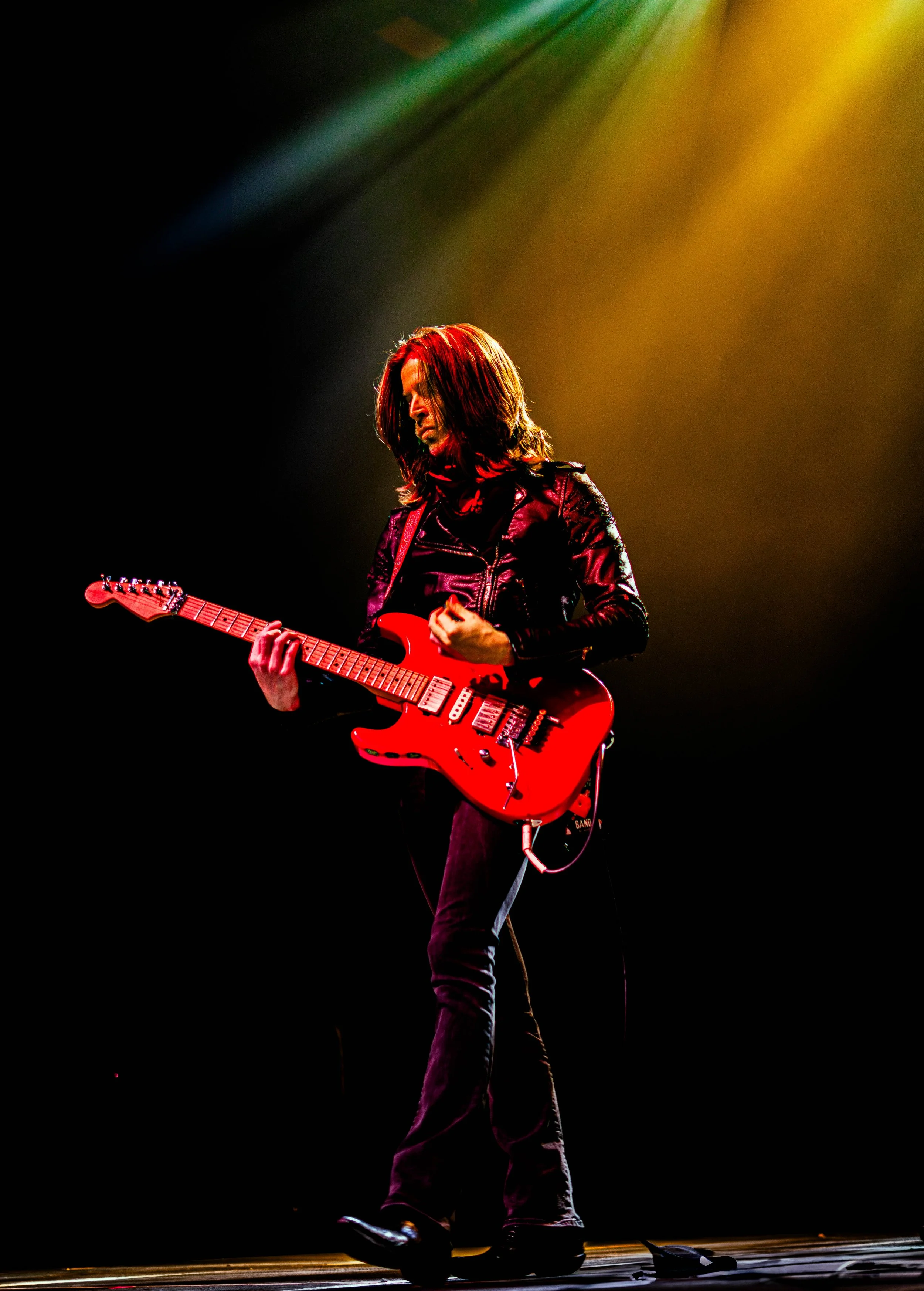 A musician playing an electric guitar on stage with colorful lights overhead.