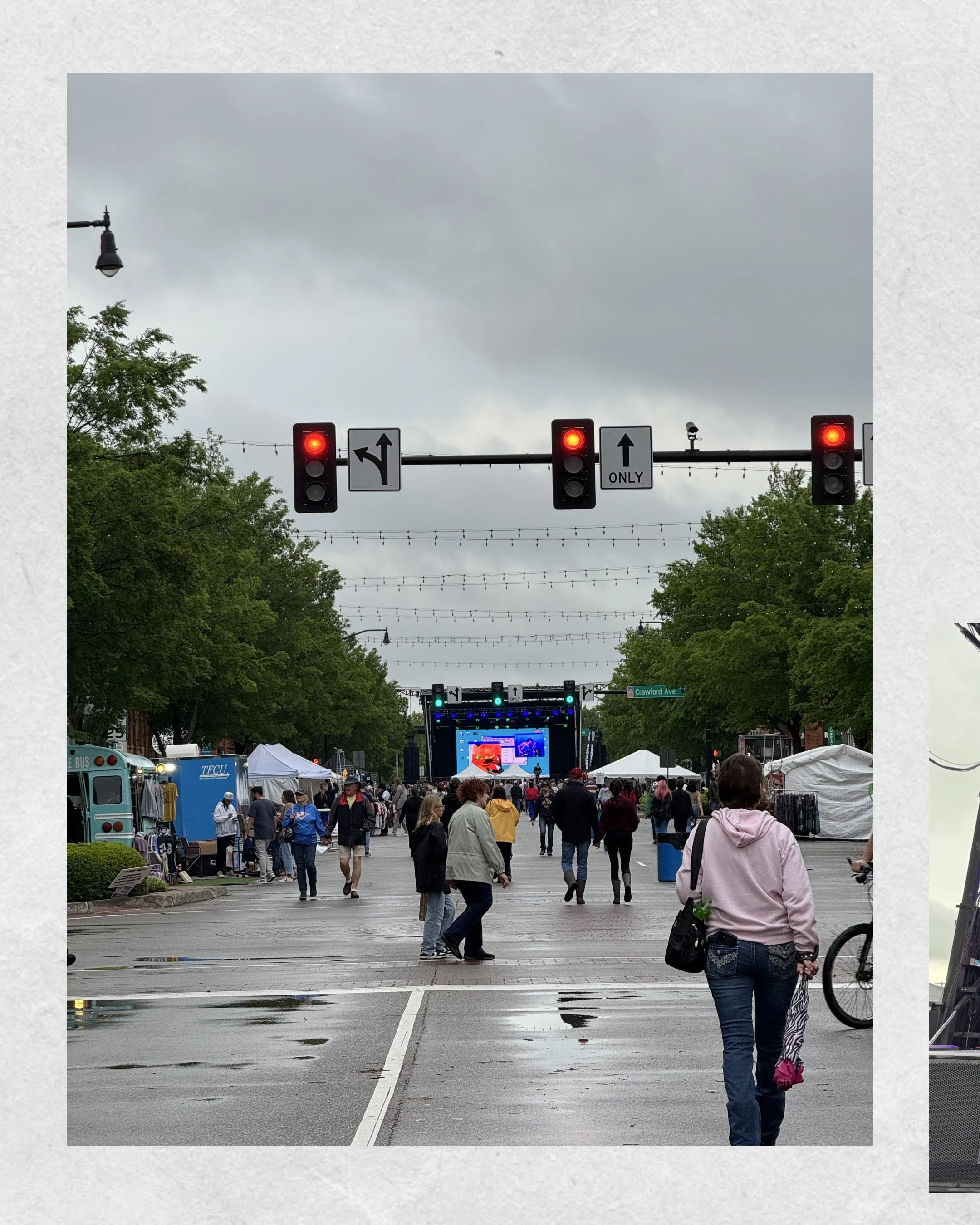 Crowd at outdoor event with stage, market stalls, and vendors on a street under overcast sky
