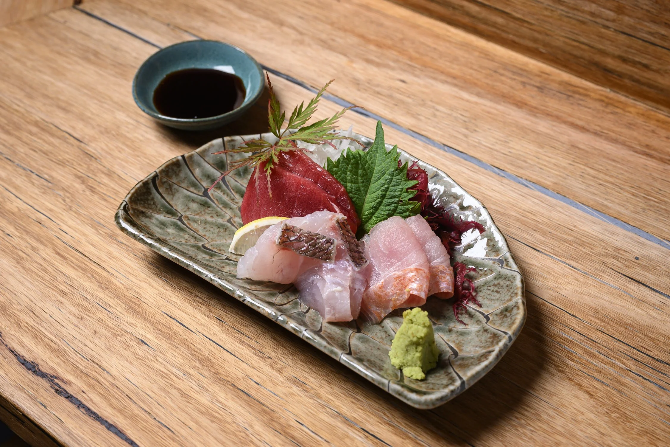 Assorted sashimi with soy sauce, wasabi, lemon, and garnishes on a ceramic plate