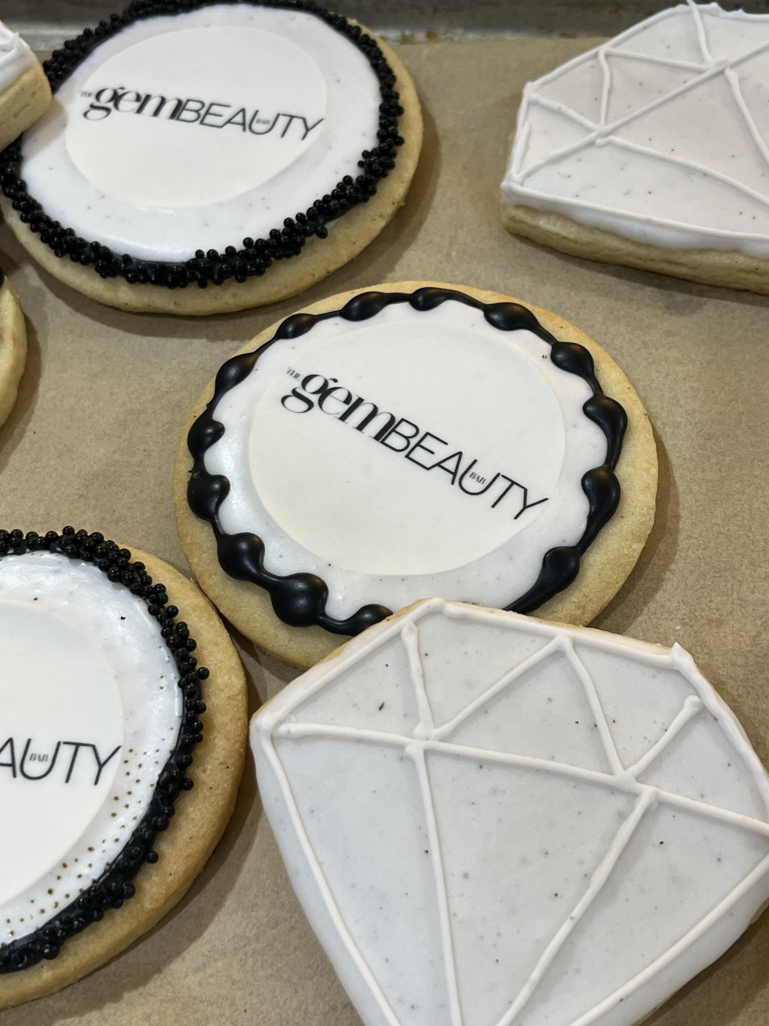 Cookies decorated with black and white icing, some displaying 'the gem BEAUTY' logo, and others with diamond-shaped designs.