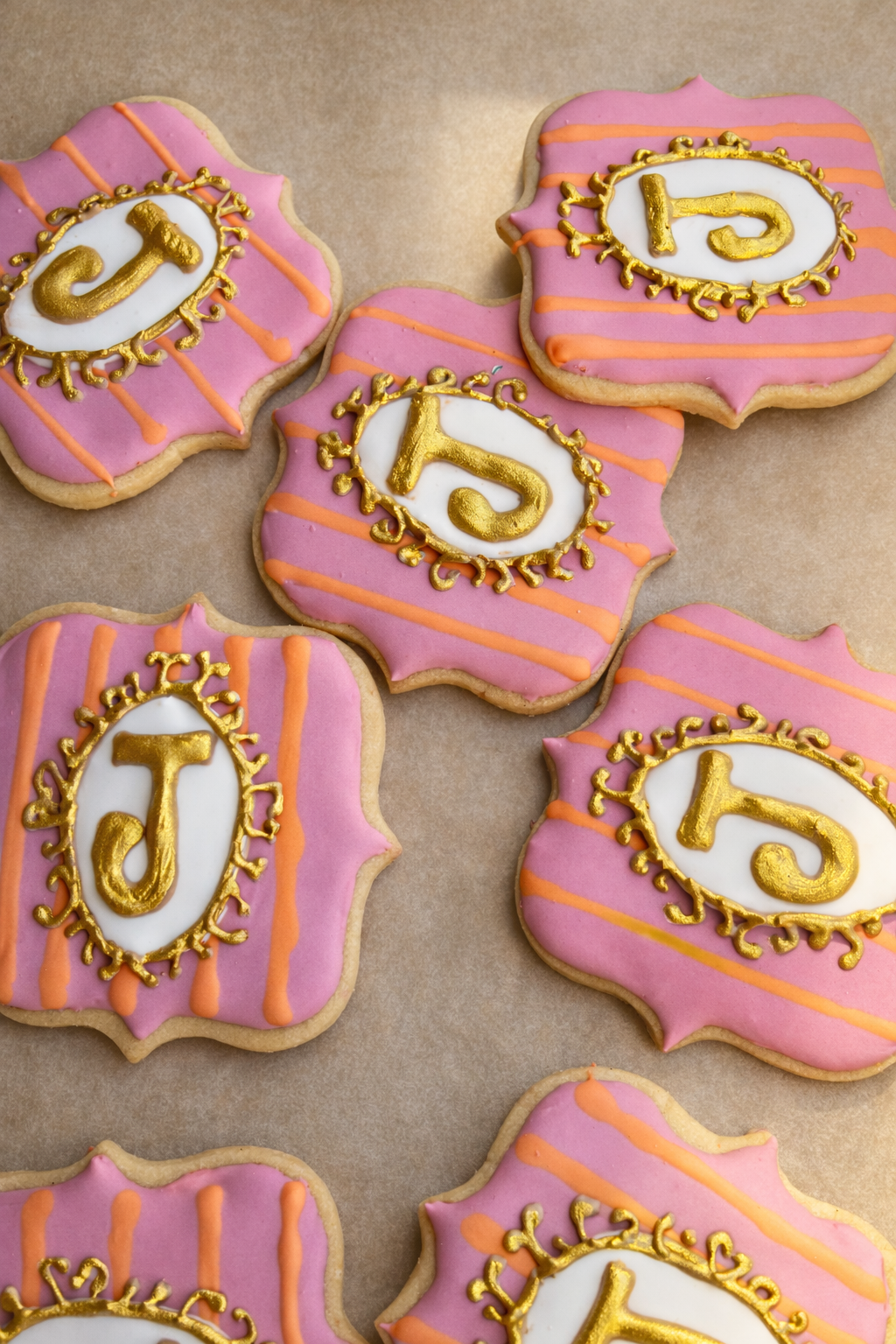 Decorative cookies with pink icing, orange drizzle, and gold-lettered initials J, 5, and 1.