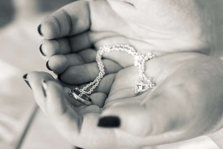 Black and White hands cupping heirloom ring on a necklace chain.