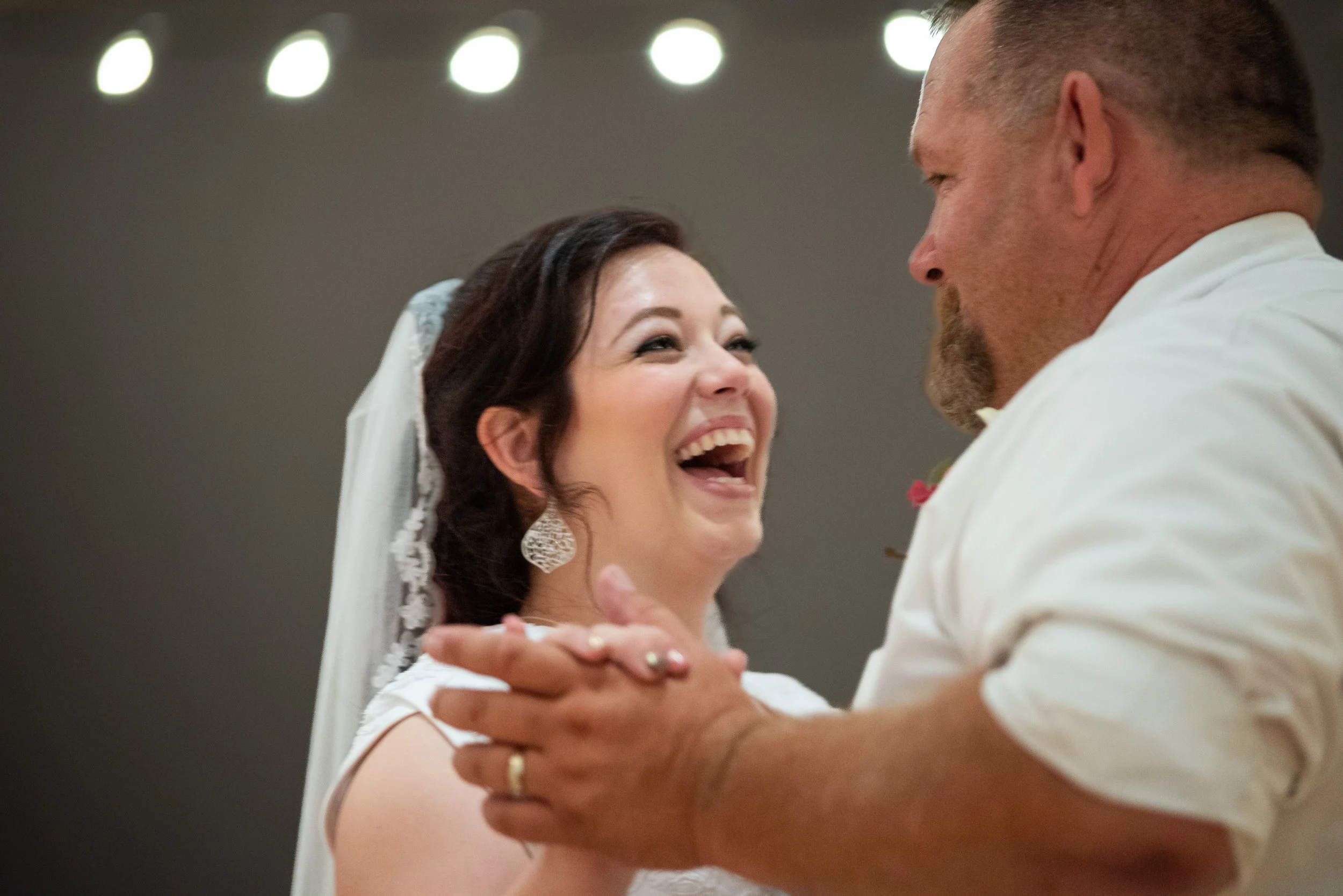 A bride and groom sharing a joyful dance, smiling and looking into each other's eyes.
