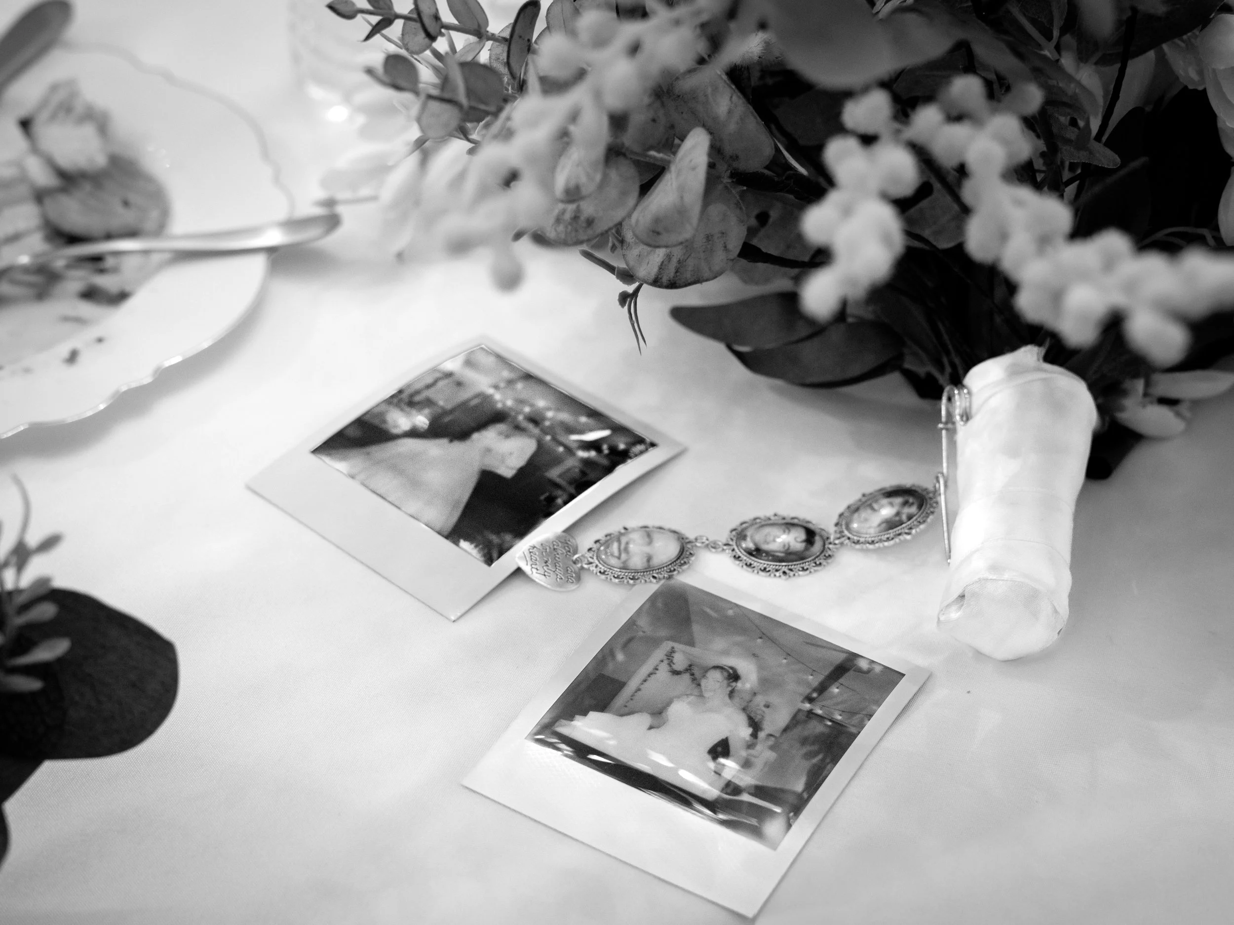 Black and white photo of a table decorated with flowers, framed photos, and small decorative objects, with a white tablecloth.