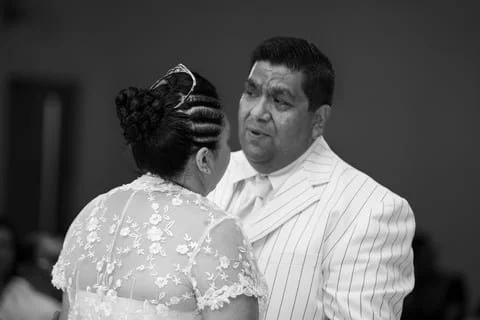 A woman in a floral dress and an updo hairstyle is talking to a man in a white pinstripe suit in a black-and-white photo.