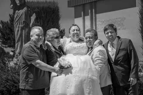 A group of five people, including a bride in a wedding dress, standing outdoors with a statue in the background.