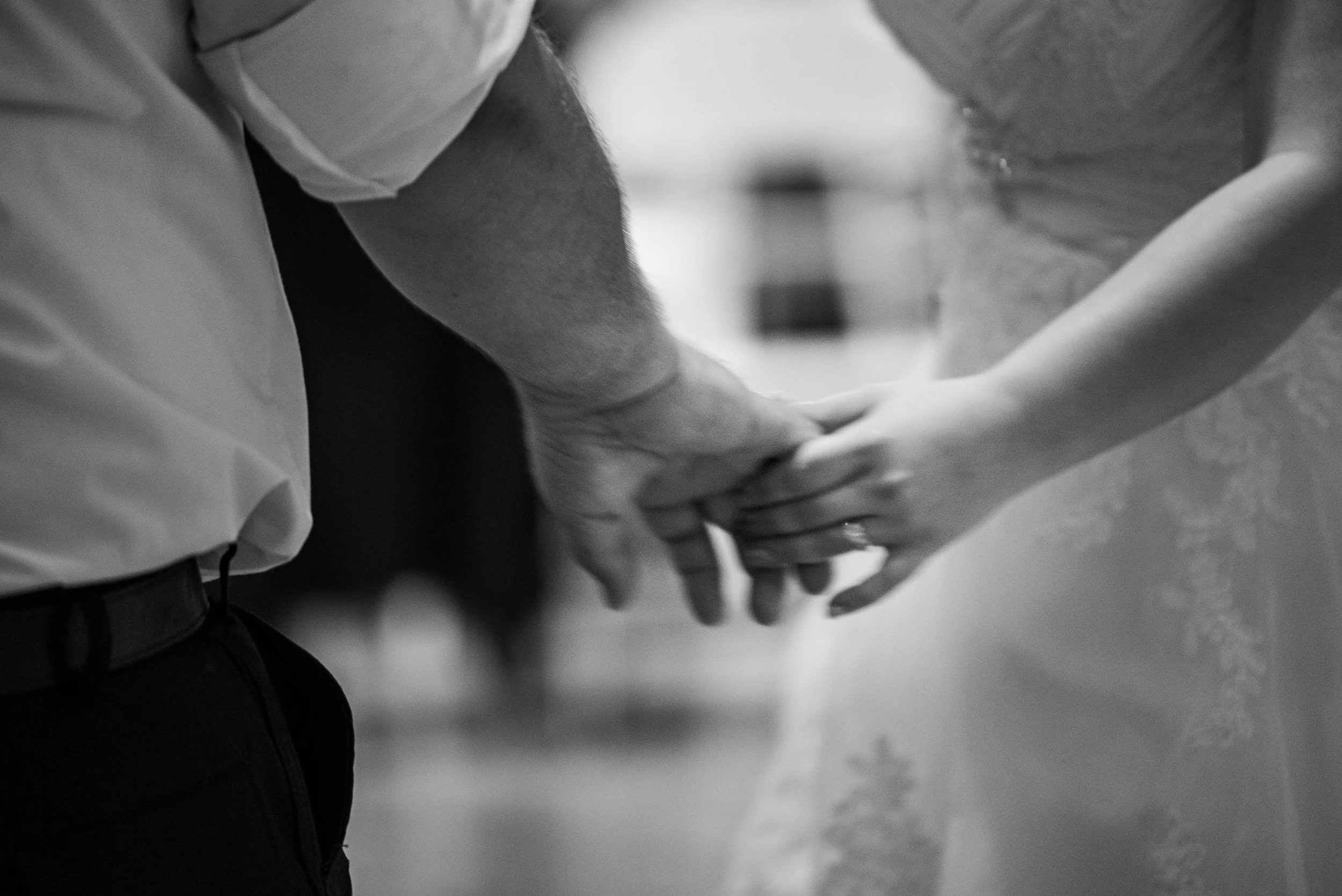 A couple holding hands, the man is wearing a white shirt and dark pants, and the woman is wearing a dress with lace details.