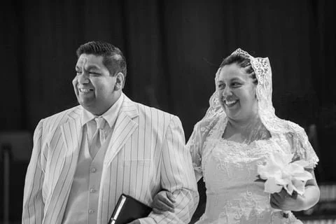 Black and white photo of a smiling bride and groom on their wedding day, with the bride holding a bouquet of flowers.