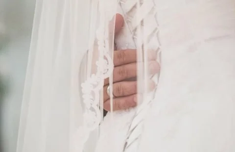 Close-up of a hand partially visible through a delicate lace curtain on a bed.