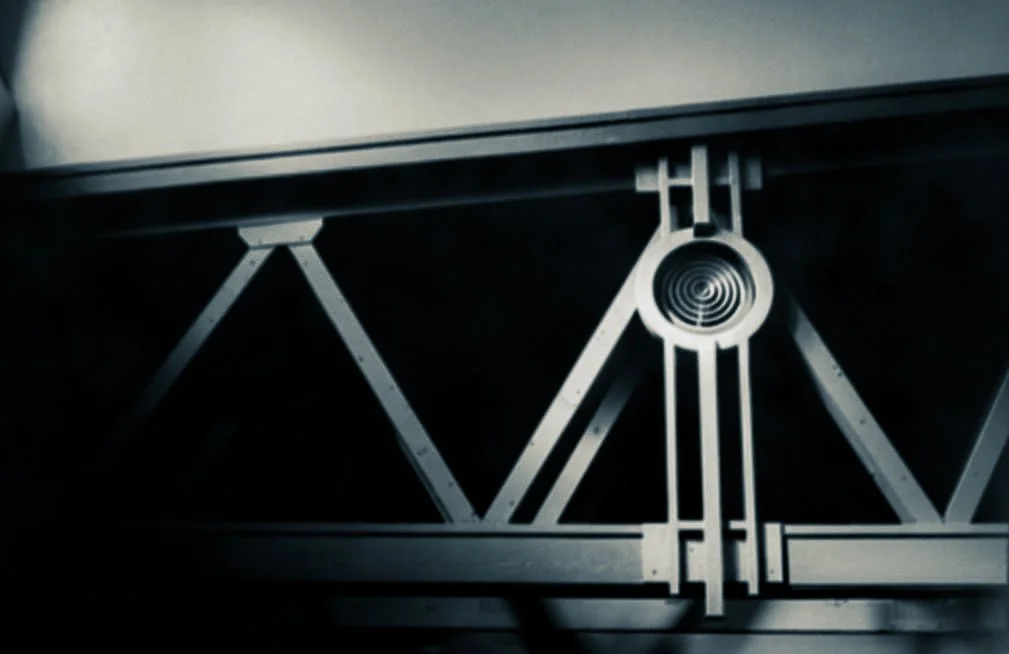 Close-up of a metallic structure, possibly a part of machinery or furniture, with a circular spiral detail and intersecting lines.