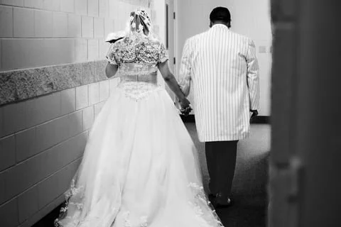 Bride and groom walking hand-in-hand down a hallway, viewed from behind.