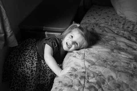 little girl leaning against bed making a silly happy face.
