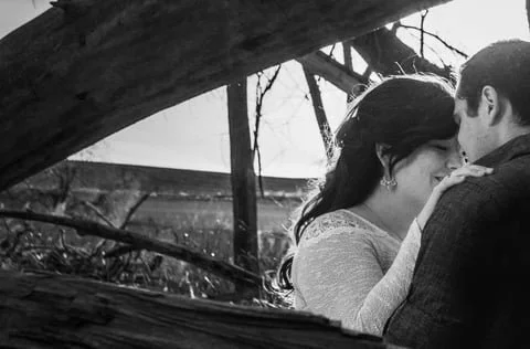 A couple kissing outdoors near fallen tree branches.