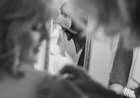 A bride and groom standing close together, with the bride holding a bouquet, in front of a mirror during a wedding ceremony or preparation.