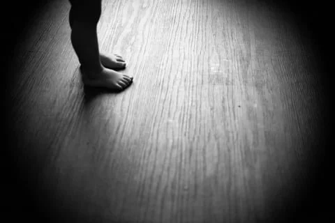 Child's bare feet standing on a wooden floor with soft lighting.