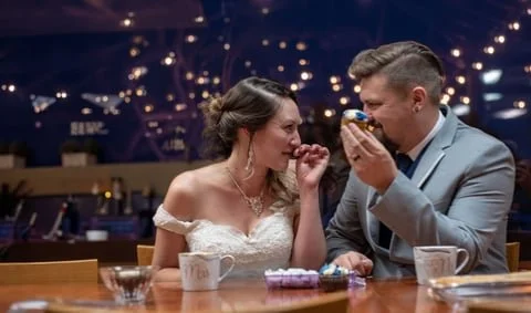 A bride and groom sharing a moment at a wedding reception, with the groom holding a ring box and both smiling.