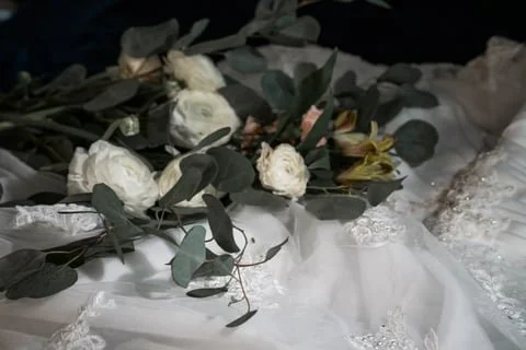 A bouquet of white flowers and green leaves on a white fabric surface with lace details.