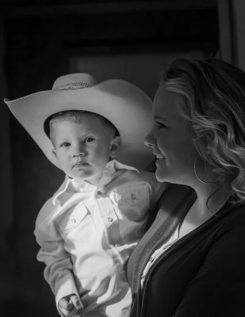 Black and white photo of a woman holding a young boy wearing a cowboy hat, both smiling.