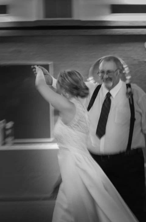 A bride dancing with an older man, possibly her father, at a wedding reception in an indoor venue.