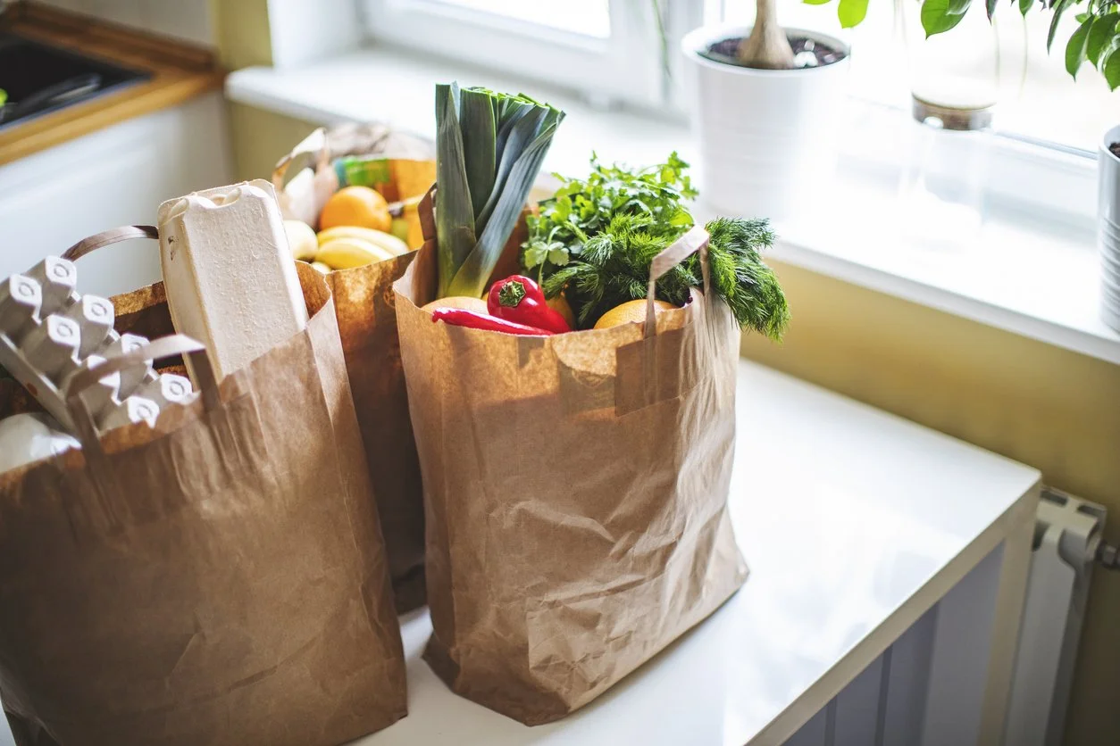 Paper grocery bags filled with fresh food on a kitchen counter, representing personal concierge errand and shopping support.