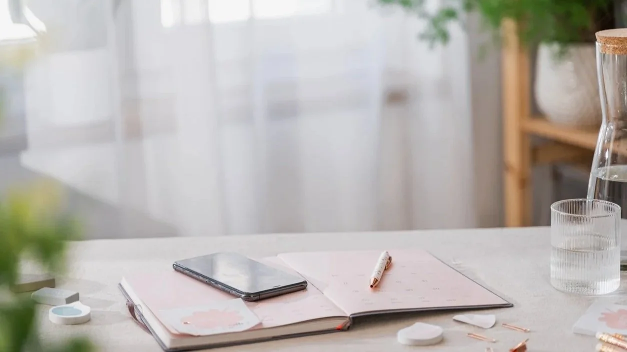 Planner and phone on a desk with a calendar open, representing personal concierge support and daily coordination.
