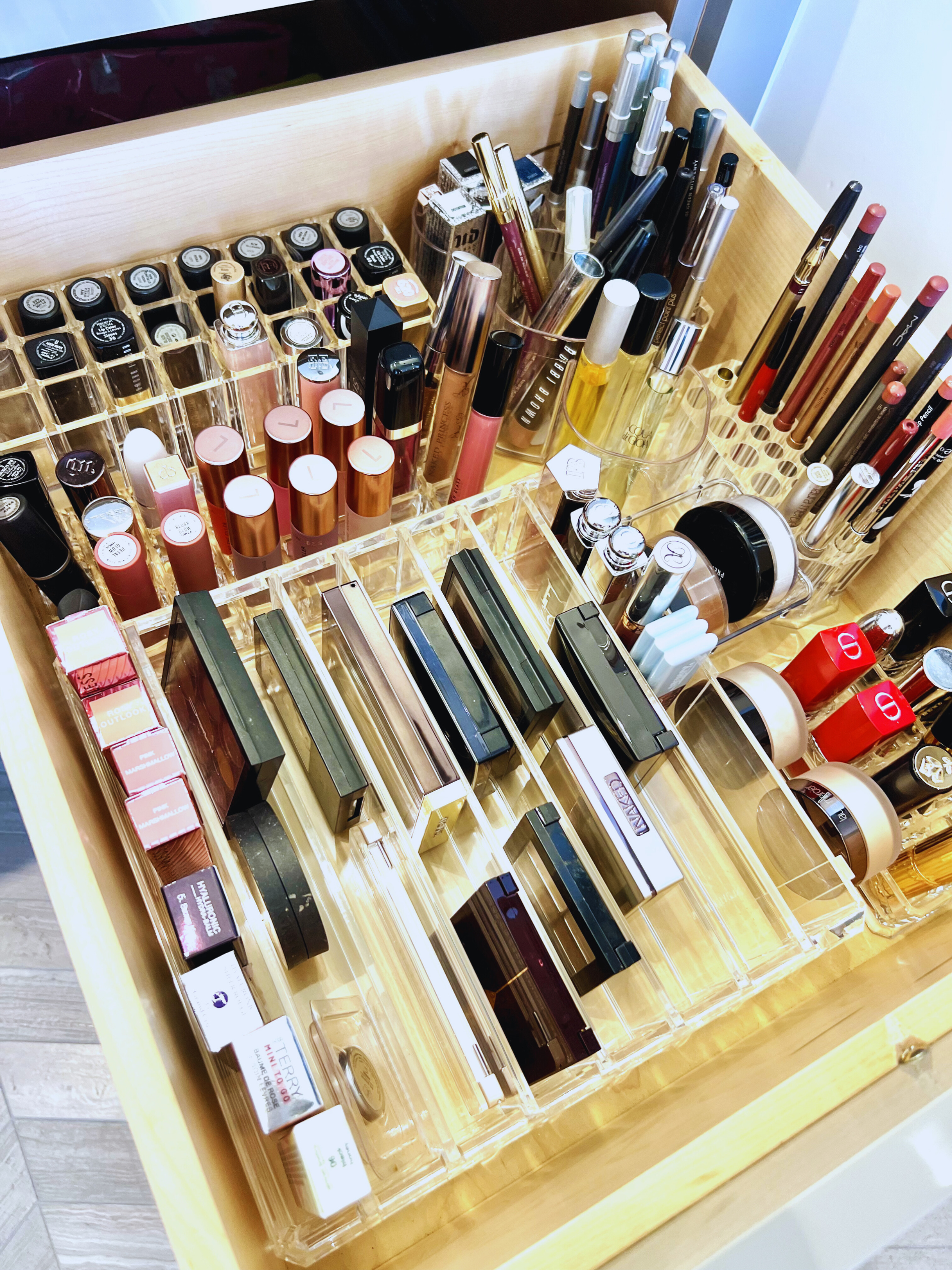 Organized makeup drawer with acrylic dividers separating cosmetics, lipsticks, and beauty products.