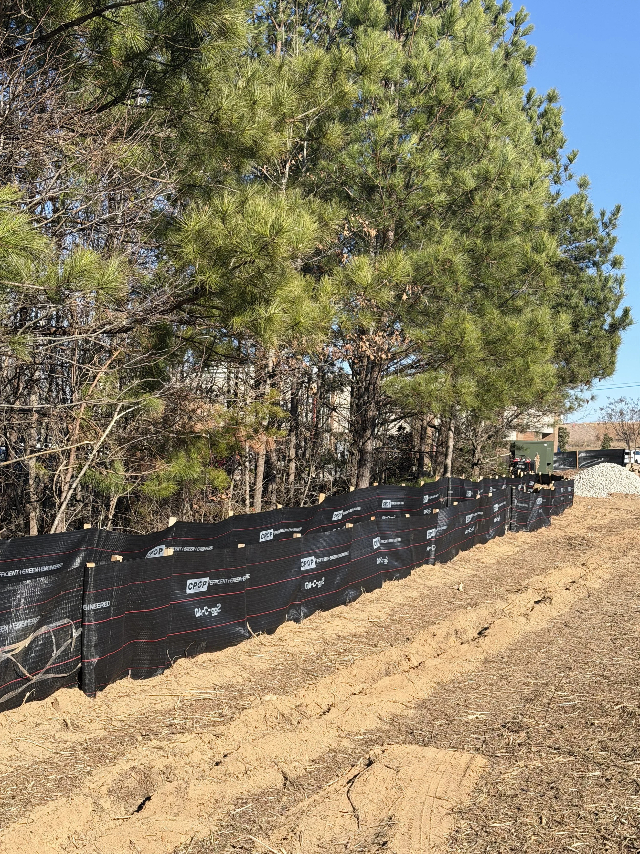 Rows of black silt fence installed along a dirt path with pine trees in the background during daytime.