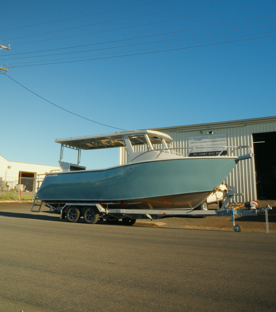 A white boat on a trailer parked outside a building labeled 'Lighthless Marine Customs & Fabrications' under a clear sky.