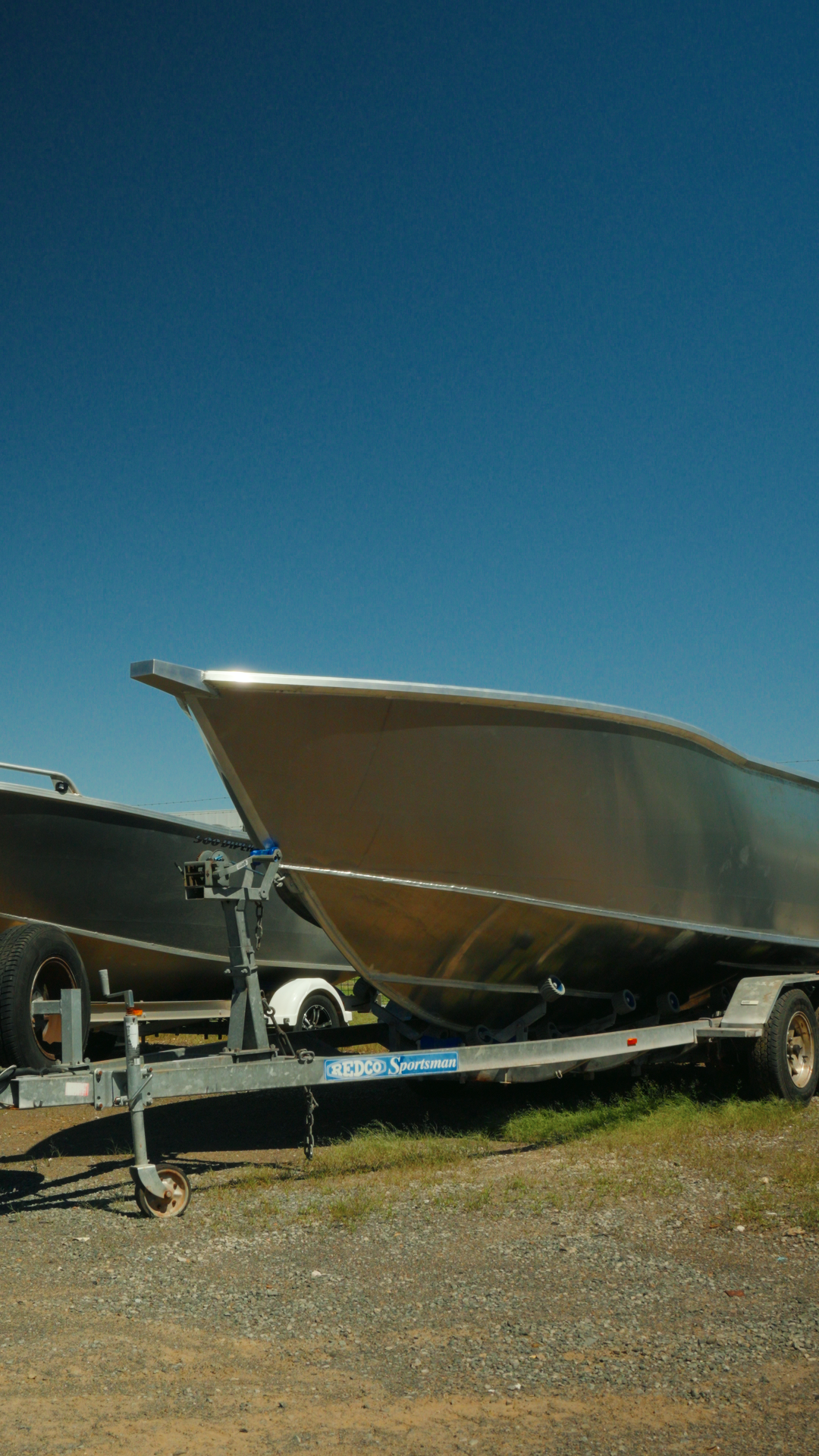 Metal boat on a trailer in an outdoor lot under a clear blue sky.