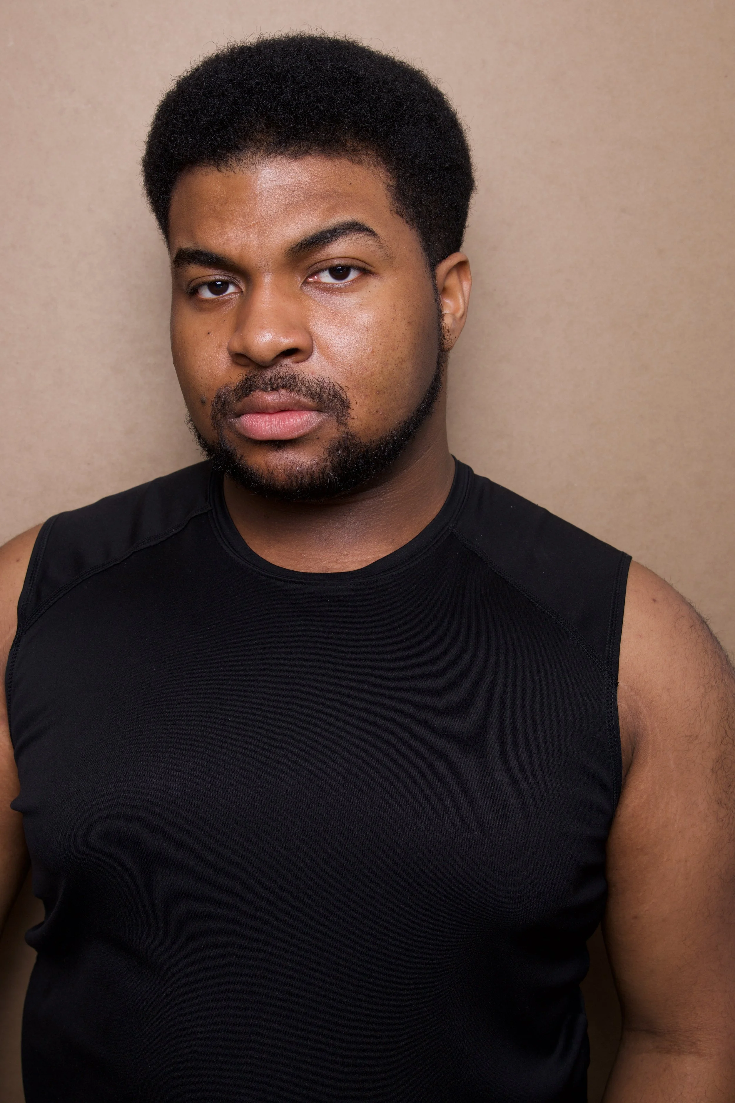 Close-up headshot of a young man, Steven Rutledge, with short curly black hair, a beard, and mustache, wearing a black tank top, standing against a beige background.

Taken by Robert Quiles (@robertredphoto on IG)