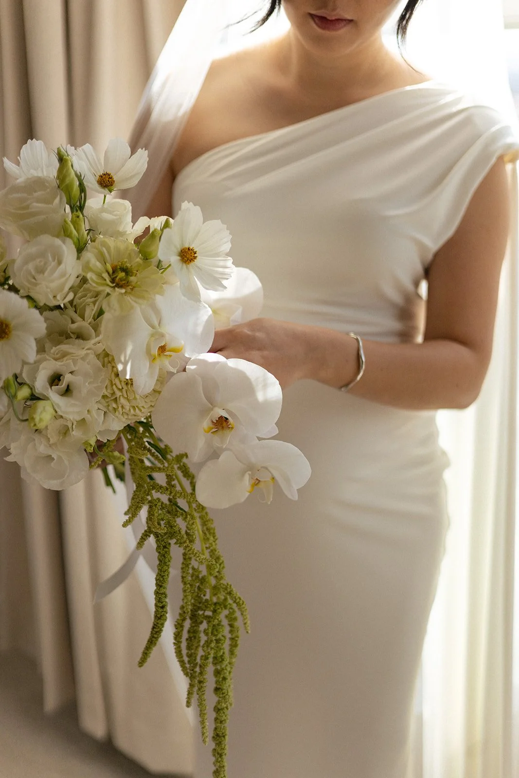 A bride in a white wedding dress holding a bouquet of white flowers, including orchids and other blooms, near her waist.