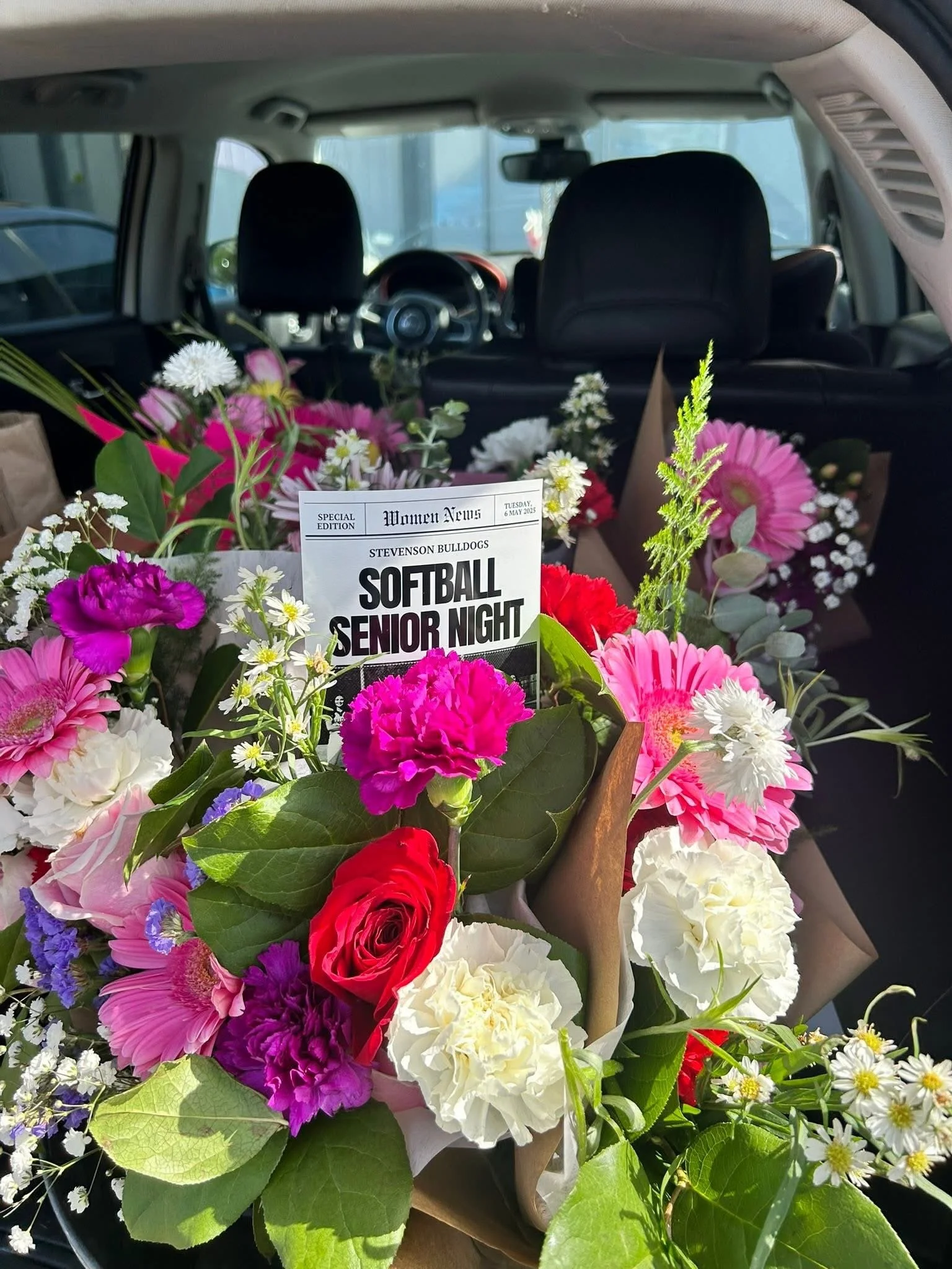 Colorful bouquet of flowers inside a car, with a flyer for a softball senior night event from Stevenson Bulldogs.