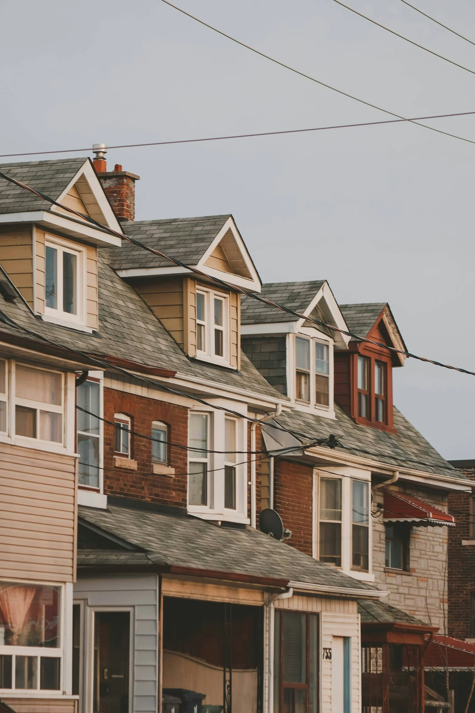 Close-up view of colorful, multi-story urban houses with various window styles and roof shapes, some with dormer windows, under a cloudy sky.