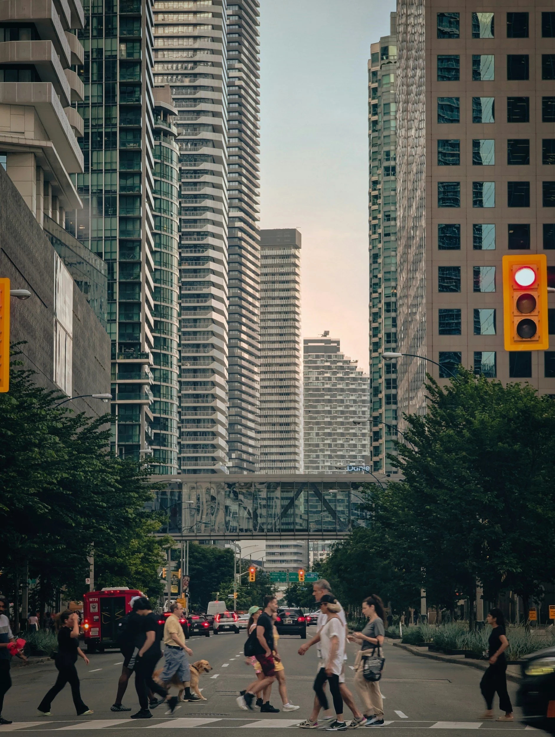 People crossing a city street with tall buildings and traffic lights in a downtown area.