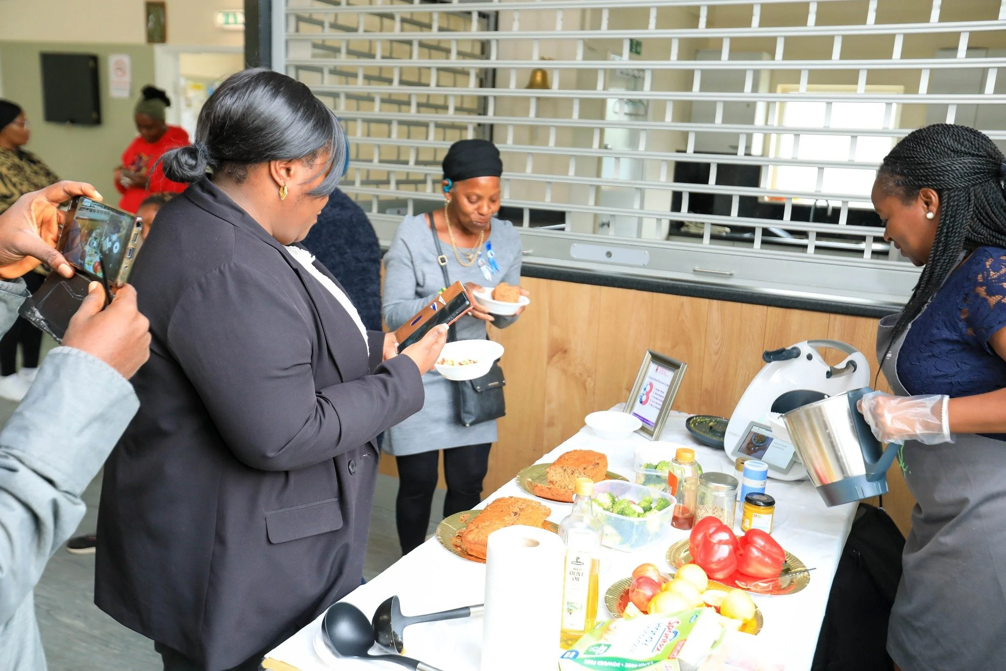 Women gathered around a table at a food event, serving and examining various dishes and ingredients.