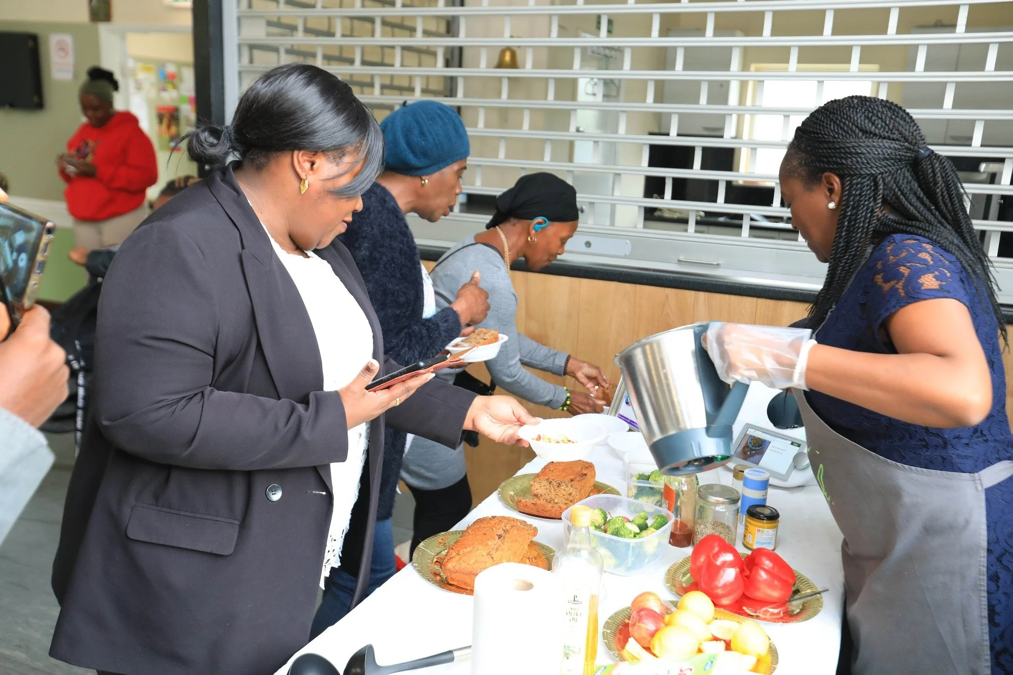 People in line at a food table with various dishes, including fried fish, vegetables, and condiments, in a community setting.