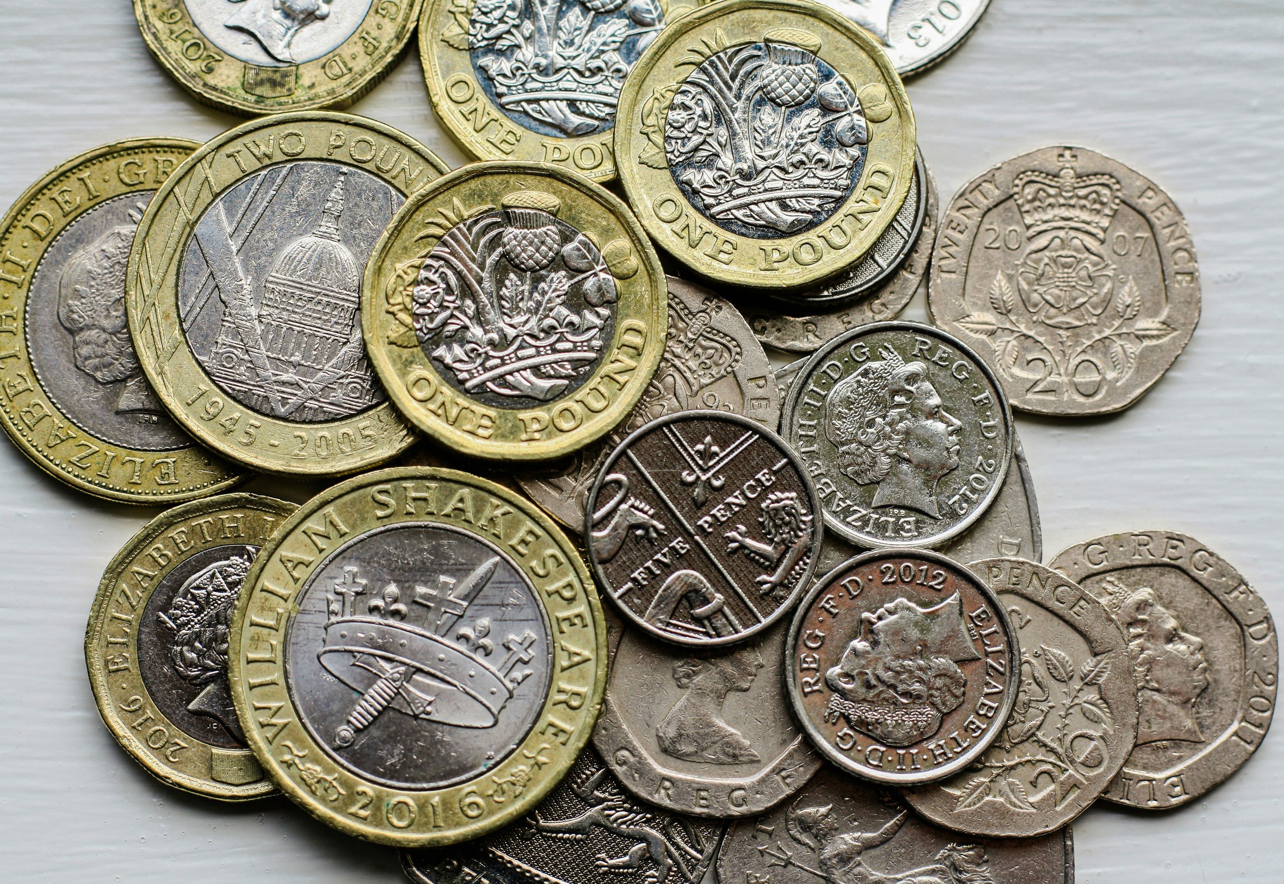 A collection of British coins, including two-tone £2 coins, silver 20 pence, and other assorted coins with various designs and denominations.