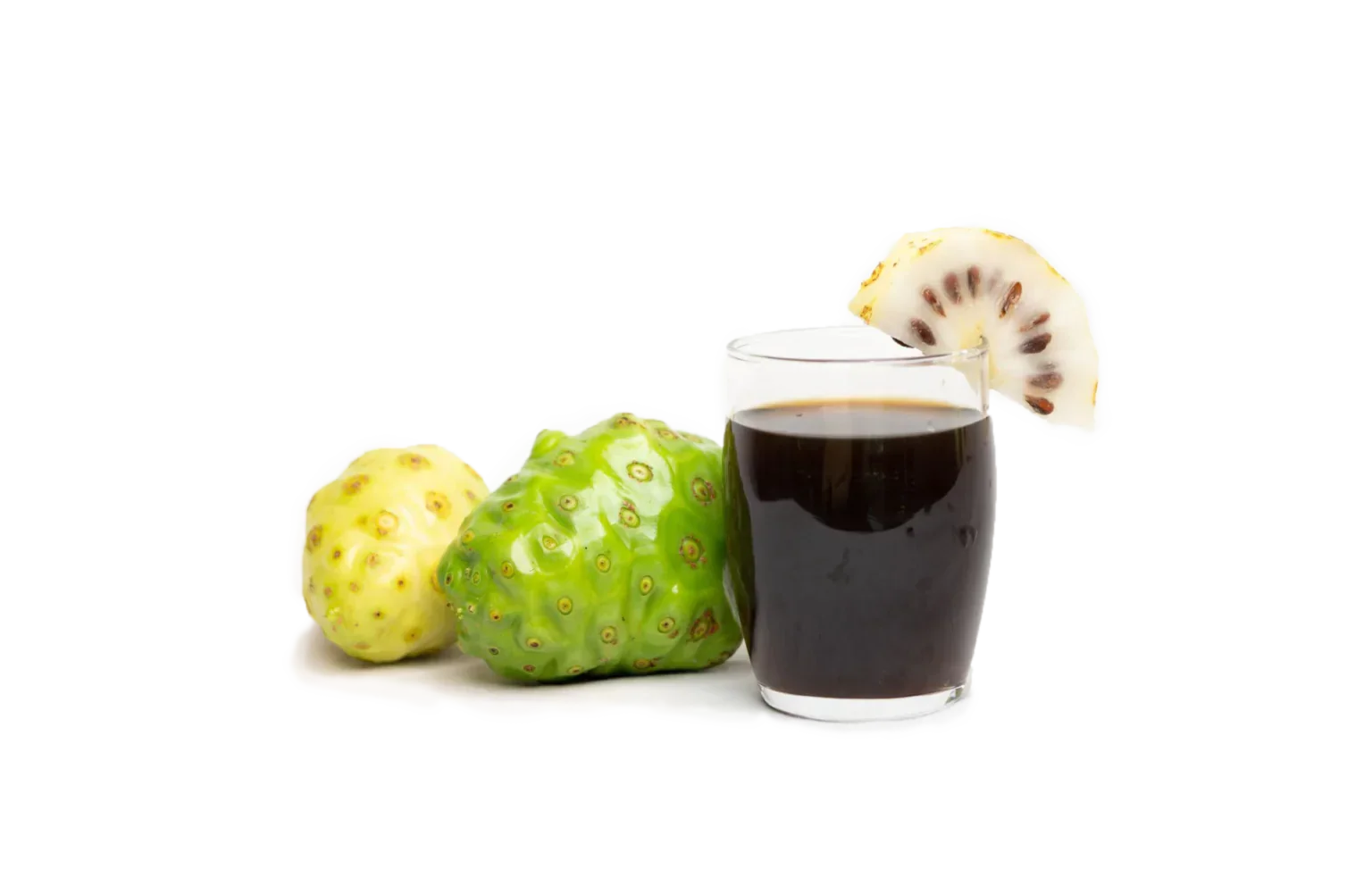 A glass of black juice with a slice of white dragon fruit on the rim, placed next to two non-typical fruits, one yellow and one green, resembling wild fruits or exotic varieties.