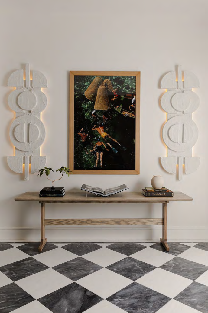 Interior view of a modern minimalist wall decor with a wooden console table, a large framed aerial photo of people floating in water, and white decorative wall panels with LED lighting, on a black and white checkered marble floor.