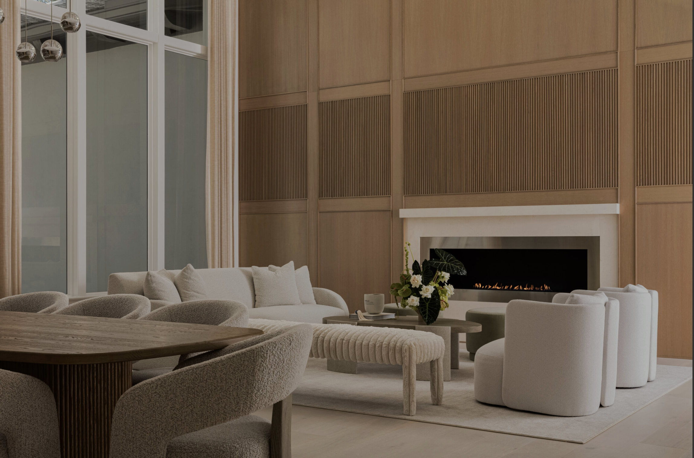 Modern living room with white sofa, round white chairs, a fireplace, and a wooden wall, decorated with a flower arrangement on the coffee table.