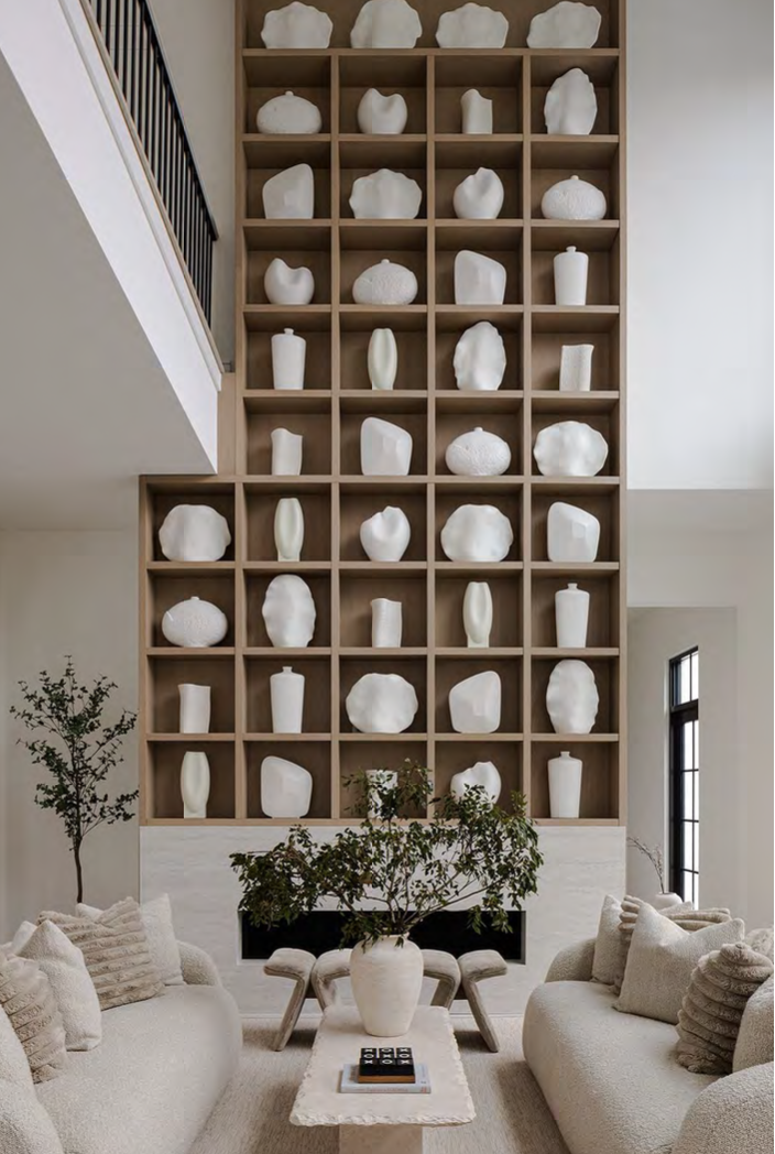 A large wall display of white ceramic vases and sculptures in a modern living room with neutral tones and minimalist decor.