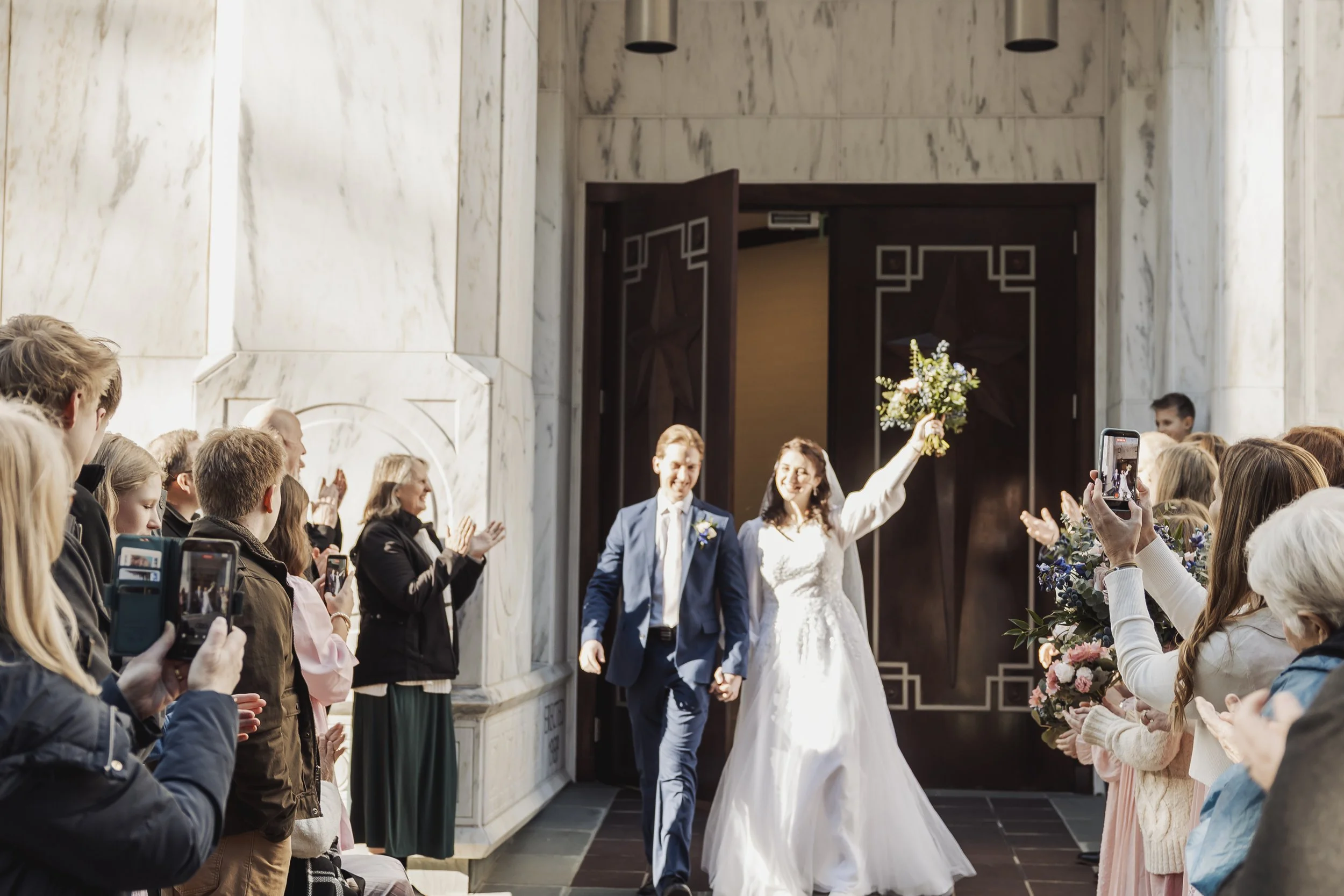 Bride and groom walking down the aisle with guests applauding and taking photos inside a church.
