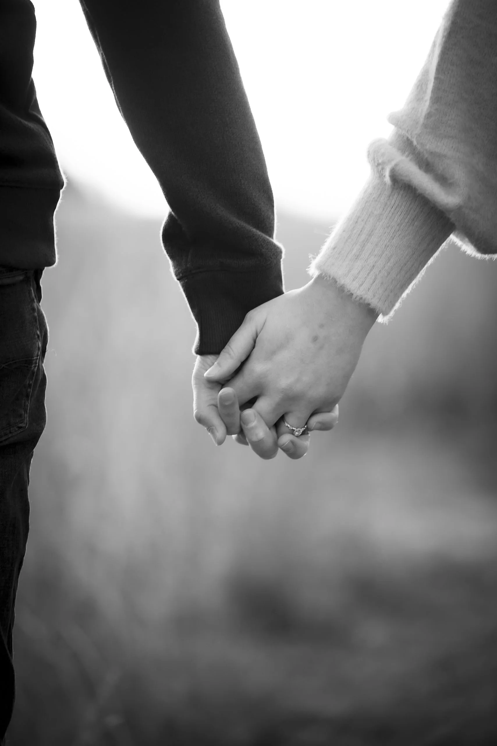 A close-up black and white photo of a couple holding hands outdoors.