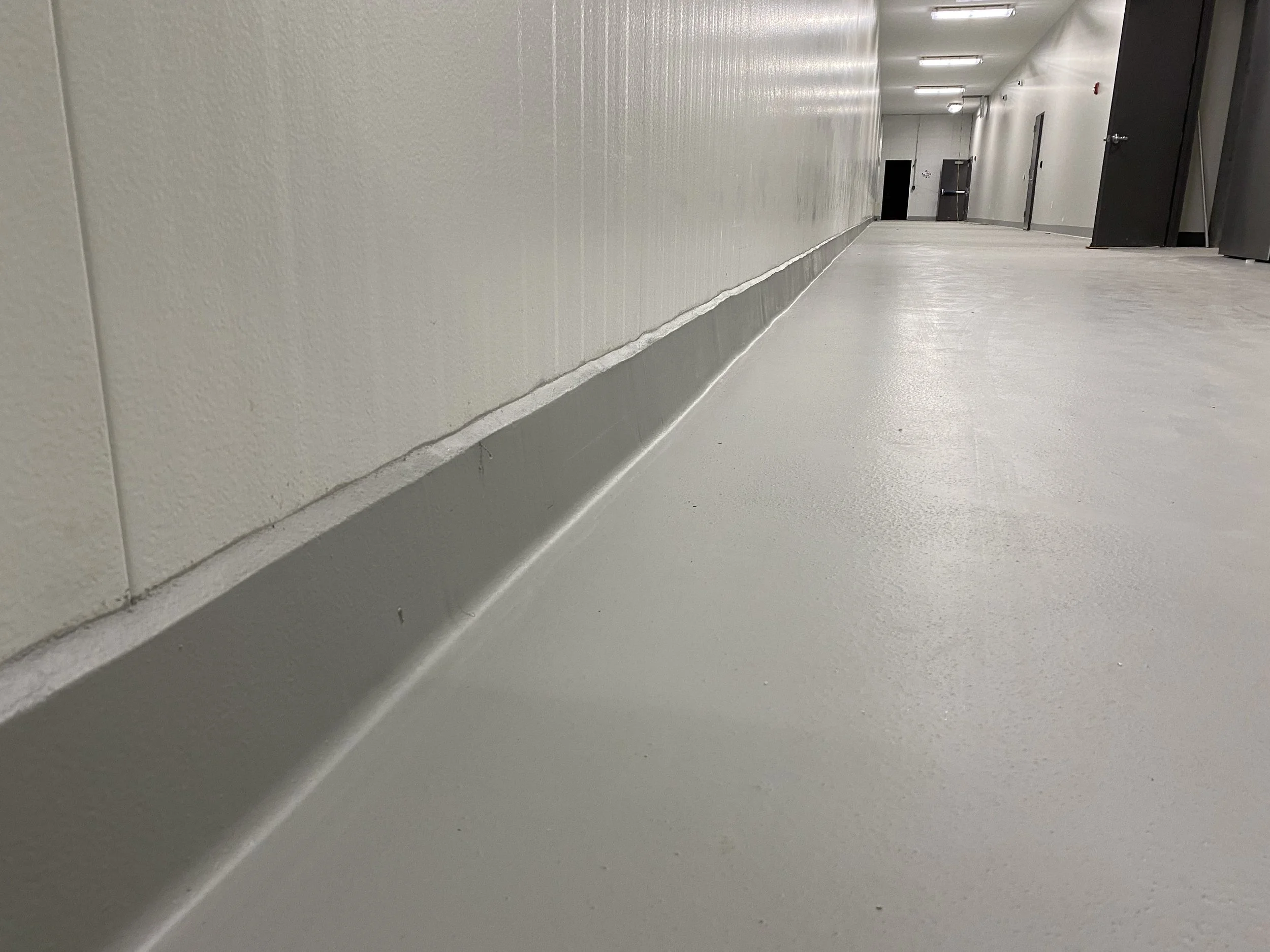 Empty hallway with white walls, a light gray floor, and multiple doors along the hallway