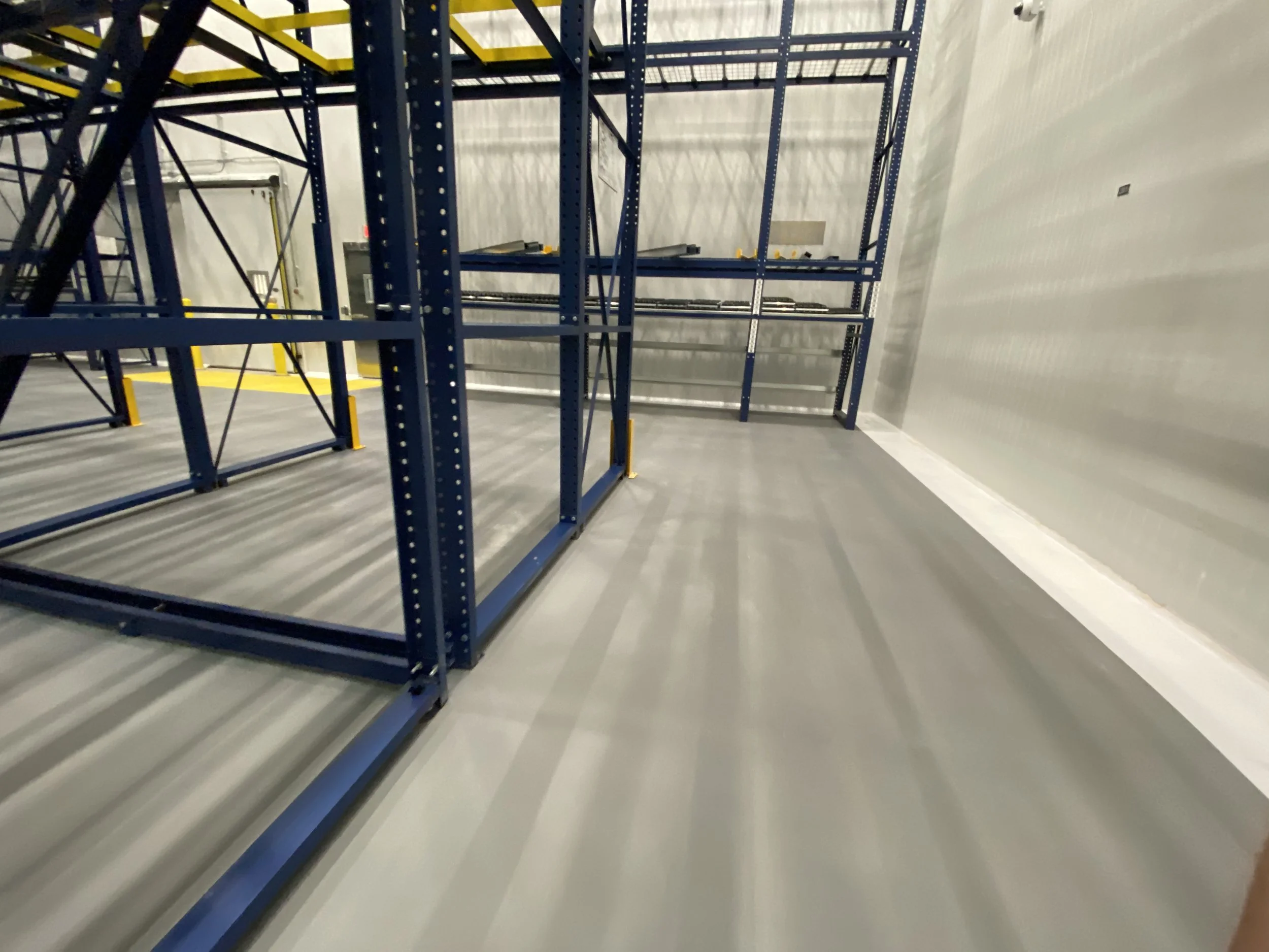 Empty warehouse or storage room with blue metal shelving units and concrete flooring.