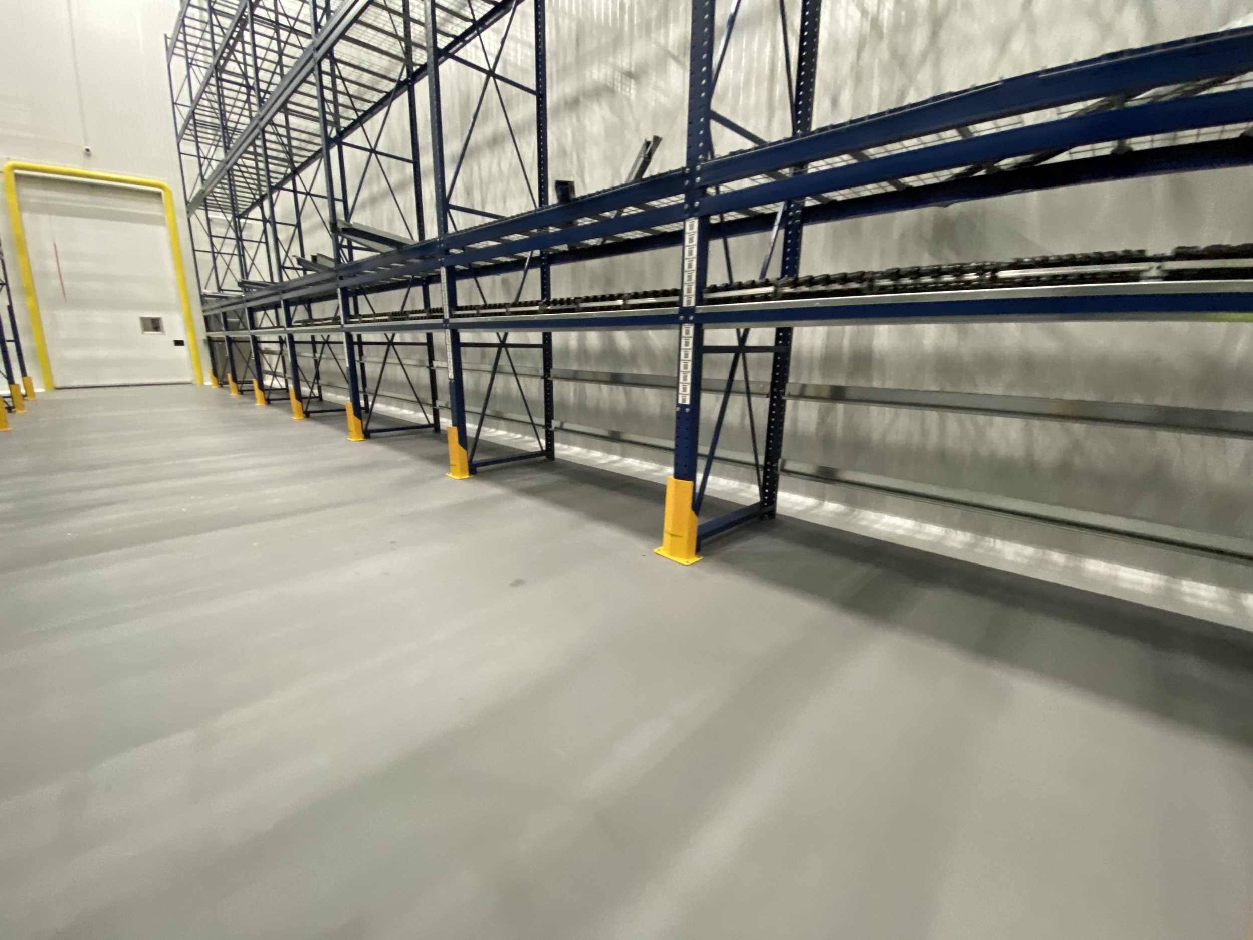 Empty industrial warehouse with metal shelving units and yellow safety barriers.