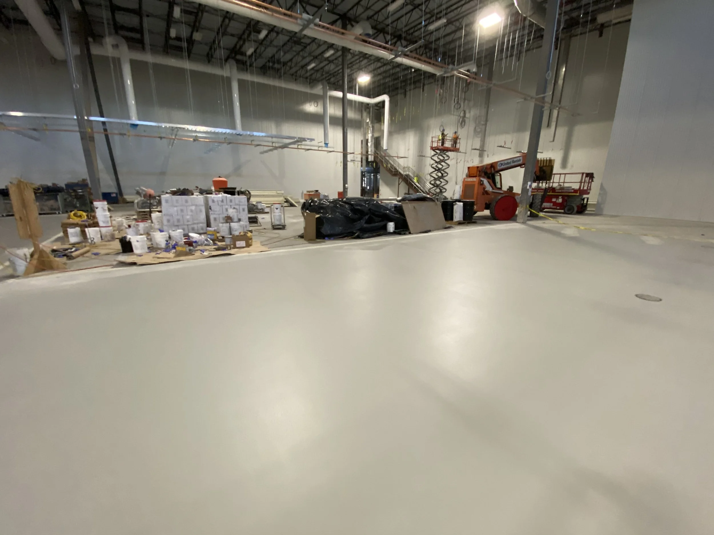 Construction site inside a large warehouse with building materials, construction equipment, and scaffolding.