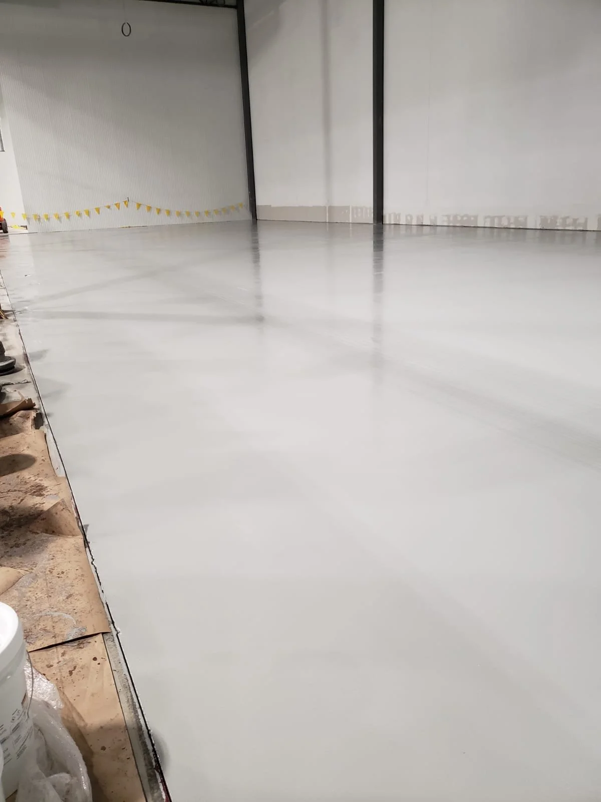 Empty industrial warehouse with freshly painted white concrete floor and some construction materials along the left side.