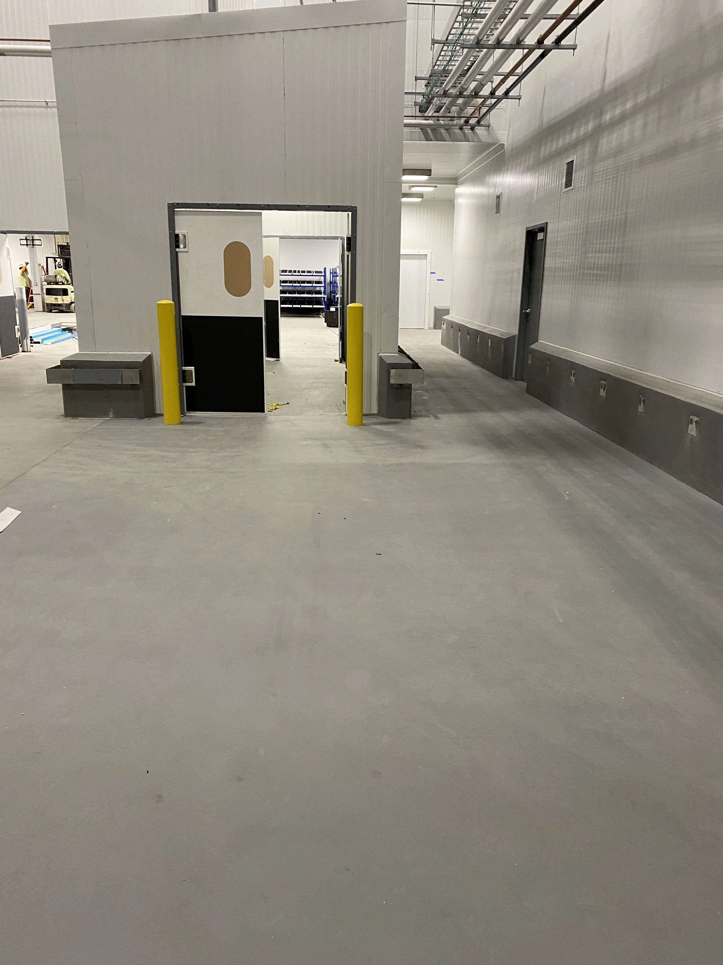 Empty indoor loading dock area with two yellow bollards, two concrete benches, and a small enclosed door.